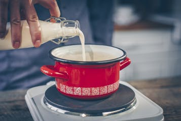 Milch wird in einem roten Topf auf einer Kochplatte aufgekocht