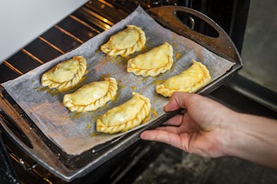 Die Empanadas liegen auf einem Backblech und werden in den Ofen geschoben
