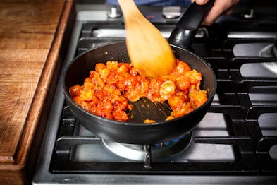 Tomaten und Zwiebeln werden in einer schwarzen Pfanne auf einem Gasherd gebraten