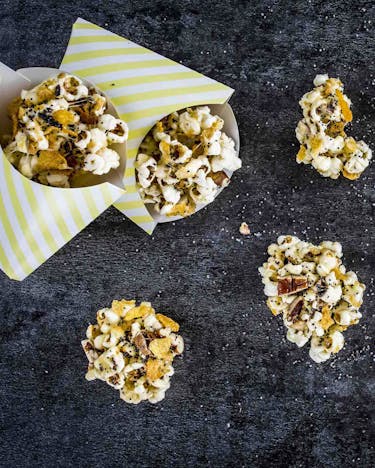 Würzige Popcorn-Kekse in gestreiften Pommestüten auf dunklem Untergrund.