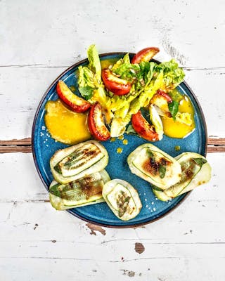 Vegane Saltimbocca aus Kohlrabi mit Salbei und Salat auf blauem Teller und hellem Holzuntergrund.