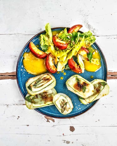 Vegane Saltimbocca aus Kohlrabi mit Salbei und Salat auf blauem Teller und hellem Holzuntergrund.