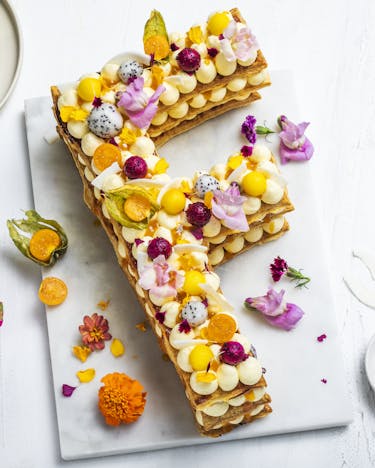 Letter Cake in F-Form für "FOODBOOM" mit bunten Früchten vor hellem Hintergrund