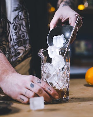 Eine Hand füllt Eiswürfel in ein Rührglas.