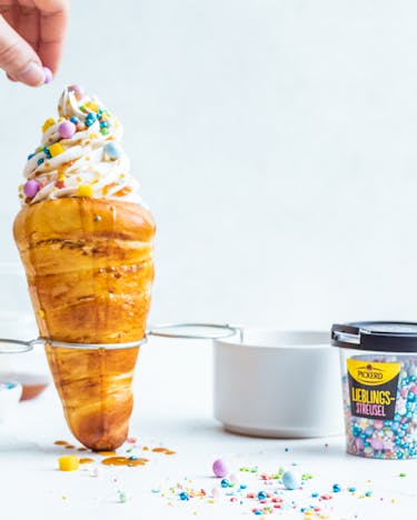Zwei Chimney Cakes mit Frozen Yoghurt und bunten Zuckerstreuseln vor hellem Hintergrund