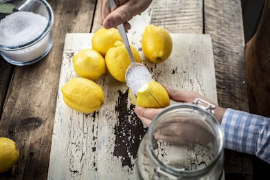 Eingeschnittene Zitrone wird mit einem Esslöffel mit Salz gefüllt. Daneben liegen weitere Zitronen und eine Schale mit Salz.