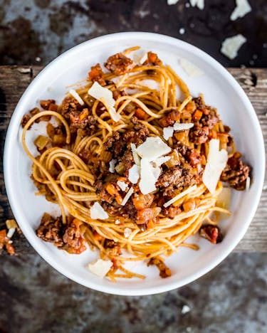 Spaghetti Bolognese auf weißem Teller, daneben Besteck mit aufgedrehten Spaghetti.