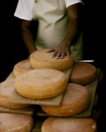 Viele große runde Käse-Laibe mit oranger Rinde auf Holzbrettern gestapelt