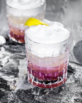 Ein Glas mit einem Soft Ice Cocktail steht mittig im Bild, am Glasrand eine Zitronenzeste