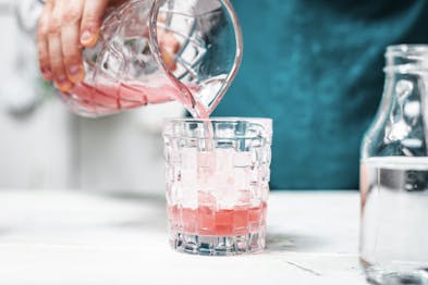 Der pinke Drink wird in ein Glas mit Eiswürfeln gegossen