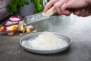 Grana Padano mit Käsereibe auf Teller reiben