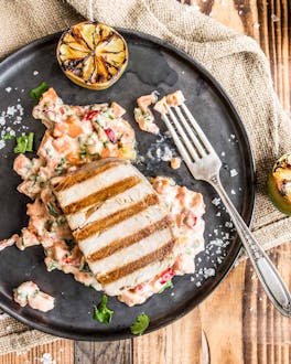 Gegrilltes Thunfischsteak an Papaya-Meerrettich-Salat und gegrillter Limette auf dunklem Teller und hellem Holzuntergrund