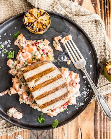 Gegrilltes Thunfischsteak an Papaya-Meerrettich-Salat und gegrillter Limette auf dunklem Teller und hellem Holzuntergrund
