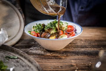 Ein Salat aus Tomate, Zwiebelringen, Avocado und Kräutern wird mit braunem Dressing übergossen