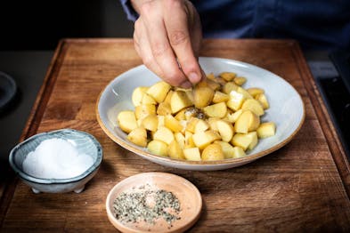 Kartoffeln in einem hellgrauen tiefen Teller werden mit Öl, Salz und Gewürzen gewürzt