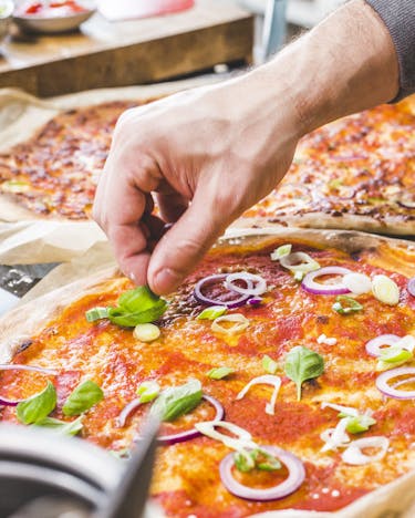 Eine Hand belegt eine Pizza mit Frühlingszwiebeln