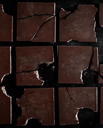 12 angebrochene Schokoladenplatten liegen auf schwarzem Untergrund