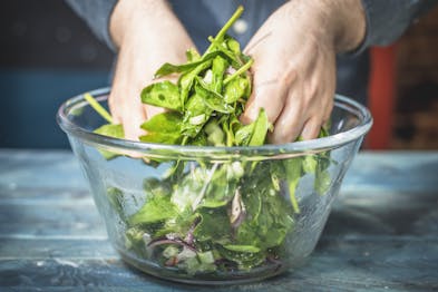 Blattspinat wird in einer Schüssel von Hand als Salat gemischt.