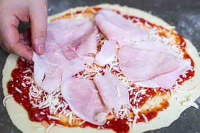 Schinken wird auf Pizza Prosciutto verteilt
