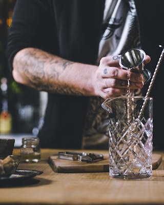 Eine Hand gießt Alkohol mit einem Jigger in ein Rührglas.
