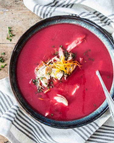 Rote-Bete-Suppe mit Hähnchen und Zironenzeseten von oben mit einem Löffel und einem Geschirrtuch