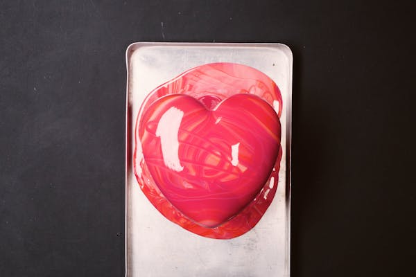 Frisch dekorierte Mirror-Glaze-Torte in rosaroter Herzform auf einem Abtropfblech
