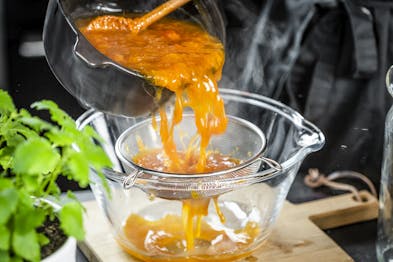 Der Aprikosensirup wird durch ein Sieb in eine Glasschüssel gegossen.