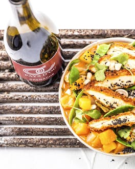 Quitten-Curry mit Cornflakes-Hähnchen und Zuckerschoten, getoppt mit schwarzem Sesam in einem Teller, daneben ein Glas Rotwein.