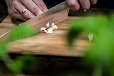 Knoblauch wird auf einem Holzbrett mit einem großen Messer gehackt