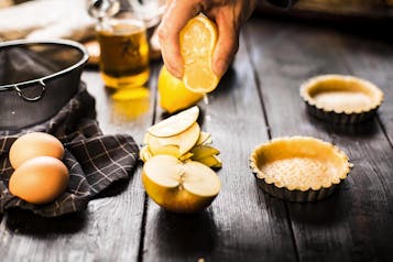 Eine Zitrone wird so ausgepresst, dass ihr Saft die dünn geschnittenen Apfelscheiben bedeckt.