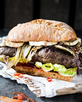 Steakburger mit Brie, Fenchel und Chili auf Zeitungspapier und Steinuntergrund.