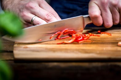 Chili wird auf einem Holzbrett mit einem Messer gehackt