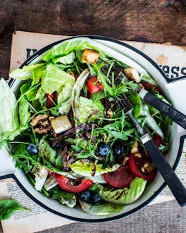 Salat aus Rucola, Romanasalat und Blattspinat mit Croûtons, Heidelbeeren und Walnüssen in einer Salatschüssel auf Zeitungspapier.