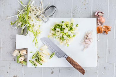 Grüner und weißer Spargel in Scheiben geschnitten, daneben Küchenabfall des Spargels, ein großes Küchenmesser und gewürfelte Zwiebel
