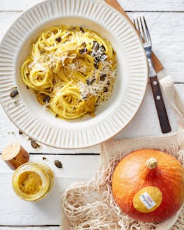 Spaghetti mit Kürbis-Pesto in einem weißen tiefen Teller. Daneben liegt ein Hokkaido-Kürbis.