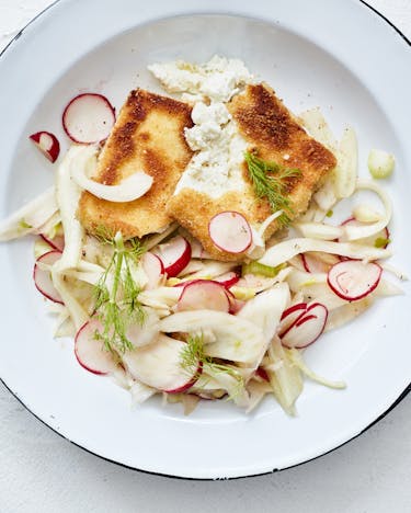 Emaille Teller mit Feta Schnitzel und Fenchel-Radieschen Salat auf weißem Tisch.