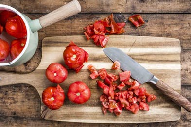 Tomaten werden auf einem Holzbrett gehäutet und gewürfelt