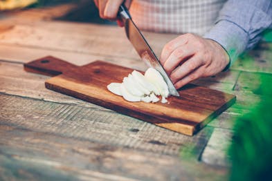 Ein Mozzarella wird auf einem Holzbrett in Scheiben geschnitten
