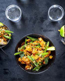 Ein Teller Asia-Salat mit Papaya, daneben stehen zwei kleinere Teller mit Salat und Garnelenspießen