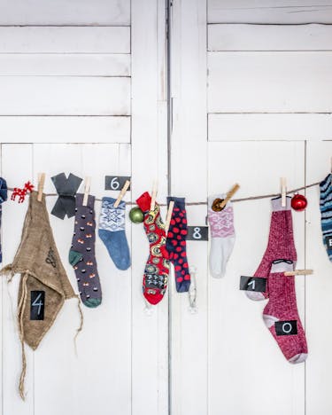 An einer Wäscheleine hängen Socken und Beutel mit Zahlen von 1 bis 24 als Adventskalender vor einer weißen Tür.