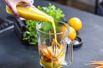Das gebackene Gemüse ist in einem hohen Gefäß. Orangensaft wird dazu gegossen.