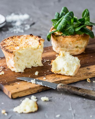 Kartoffelpüree-Muffins mit Käse überbacken und Feldsalat auf einem Holzbrettchen mit Messer