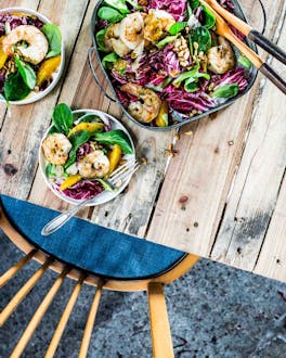 Auf einem Holztisch steht eine Schüsseln mit Salat, daneben zwei kleine Schüsseln mit Portionen