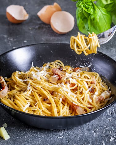 Spaghetti Carbonara in Pfanne mit Käseverpackung Giovanni Ferrari im Hintergrund