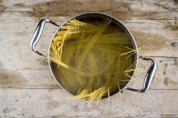Spaghetti liegen in einem Kochtopf mit Wasser auf einem Holzuntergrund