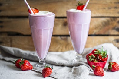 Zwei Gläser mit rosa Erdbeer-Milchshake und frischen Erdbeeren