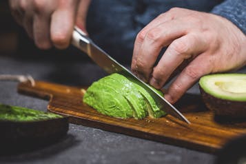 Eine Avocadohälfte wird auf einem Holzbrett in Scheiben geschnitten