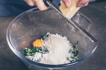 Parmesan wird für Gemüsekroketten in Schüssel gerieben