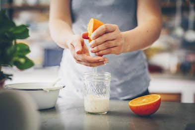 Eine Orangenhälfte wird in ein Glas mit Joghurt ausgepresst