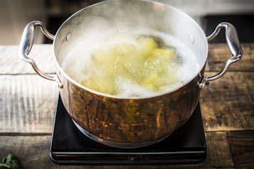 KArtoffeln werden in einem kupferfarbenen Topf auf einer Kochplatte gekocht